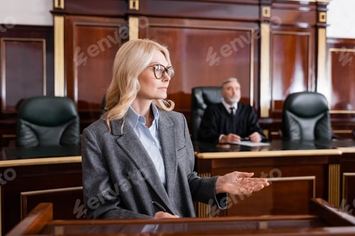 Preview: Blonde Advocate Pointing With Hand While Talking in Court Near Judge on Background