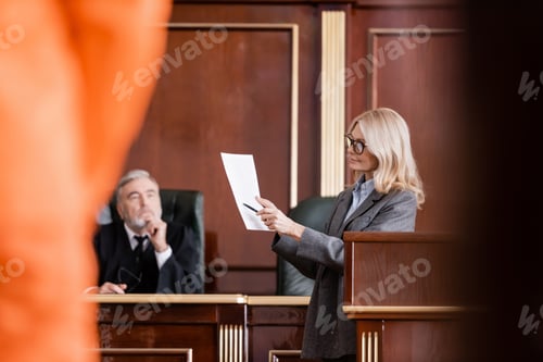 Preview: Blonde Advocate Pointing at Lawsuit Near Judge in Courtroom on Blurred Foreground