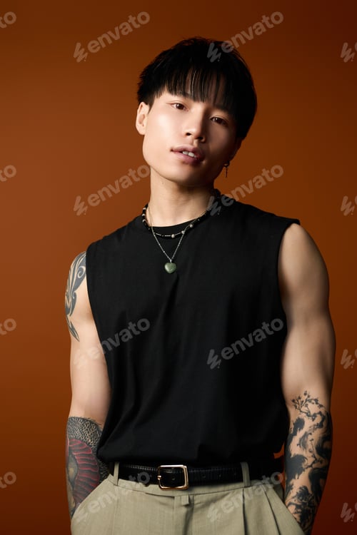 Preview: Young handsome man poses confidently against a warm orange backdrop showcasing his style and tattoos