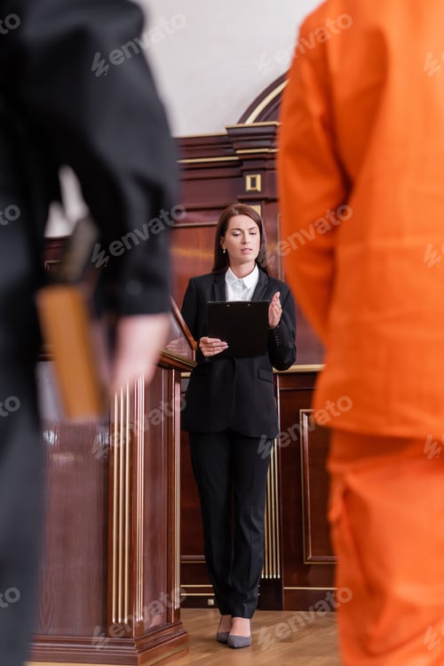 Preview: Prosecutor With Clipboard Reading Lawsuit Near Accused Man and Bailiff on Blurred Foreground