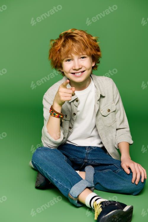 Preview: Little stylish boy showcases vibrant personality in trendy attire against bright green backdrop