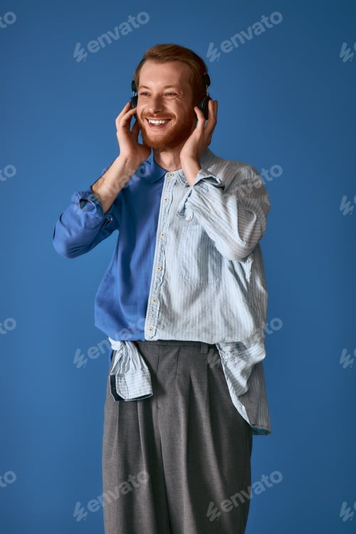Preview: Handsome red haired man enjoying music in stylish attire against a vibrant blue backdrop