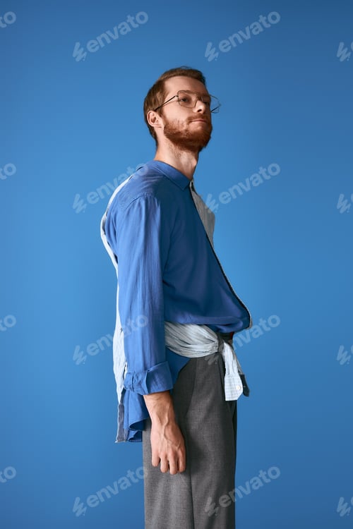 Preview: Stylish red haired man showcases modern fashion against a vibrant blue backdrop