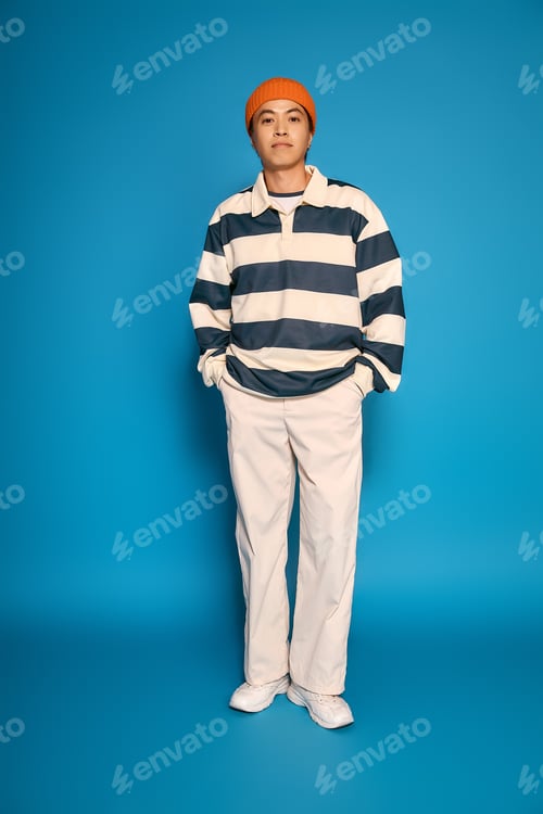 Preview: Stylish young man in striped attire poses confidently in vibrant studio setting
