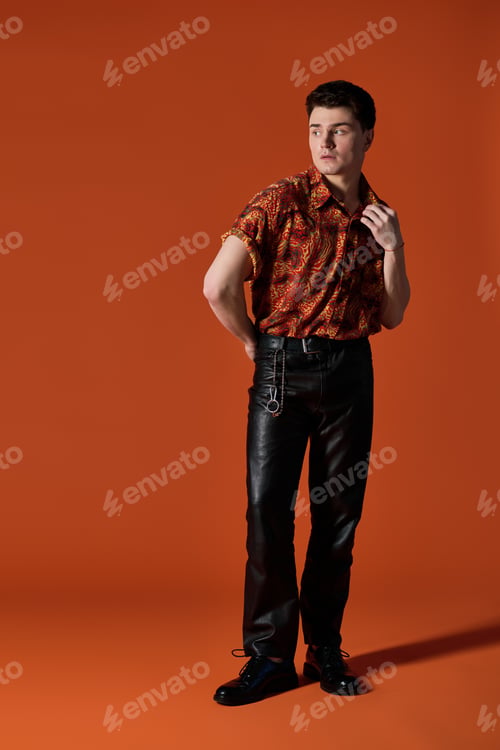 Preview: Handsome young man poses confidently against a vibrant orange background showcasing trendy fashion