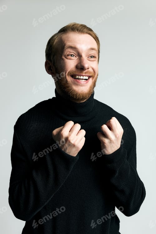 Preview: Stylish young man expresses joy in a trendy black turtleneck sweater against a simple backdrop
