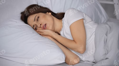Preview: Frowning Woman Lying in Bed With Closed Eyes and Suffering From Toothache