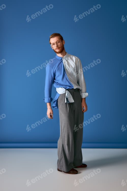 Preview: Stylish red haired man showcases modern fashion in vibrant blue setting