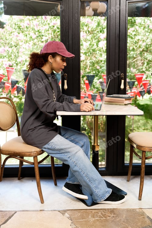 Preview: Charming young woman with curly hair focused on her laptop in a vibrant cafe setting