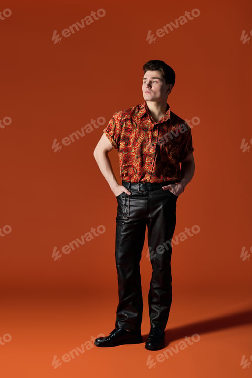 Preview: Handsome young man poses confidently against a vibrant orange backdrop in stylish attire