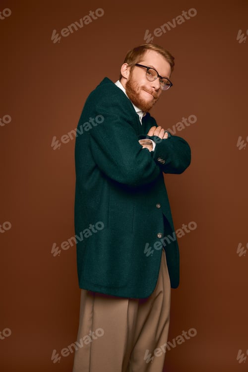 Preview: Handsome red haired man poses stylishly in smart attire against a warm brown backdrop