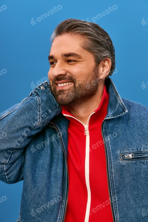 Preview: Stylish man smiling against a vibrant blue background during a sunny day in a trendy outfit