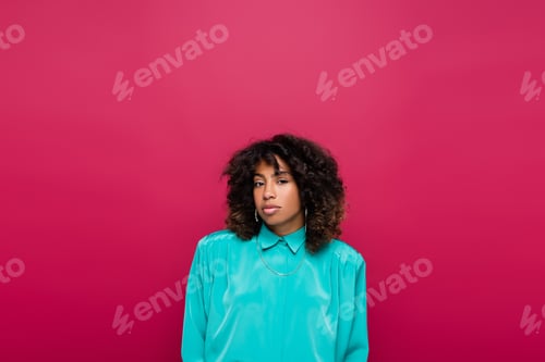 Preview: Curly African American Woman in Turquoise Blouse Looking at Camera Isolated on Pink