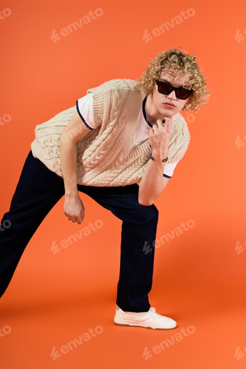 Preview: Young man with curly blonde hair showcases trendy fashion style in studio setting