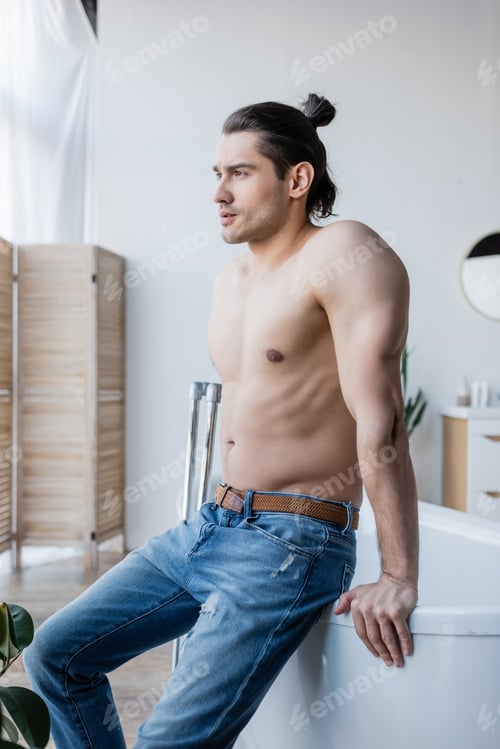 Preview: Muscular Man With Long Hair Sitting on Bathtub in Modern Bathroom