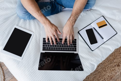Preview: Cropped View of Man Using Laptop With Blank Screen Near Gadgets and Credit Card on Bed