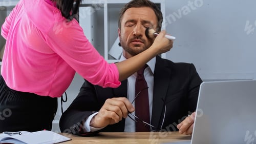 Preview: Woman Doing Makeup to Man in Suit Sitting at Desk Near Laptop