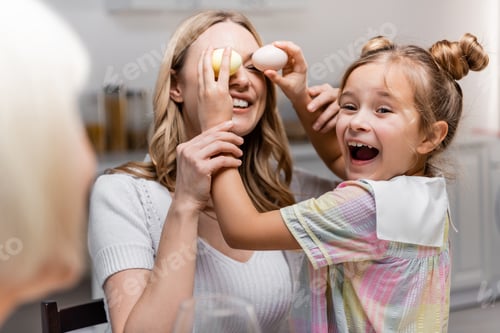 Preview: Excited Girl Covering Eyes of Mother With Easter Eggs Near Blurred Granny
