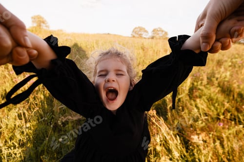 Preview: Little girl laughing while parents spin her by hands in meadow