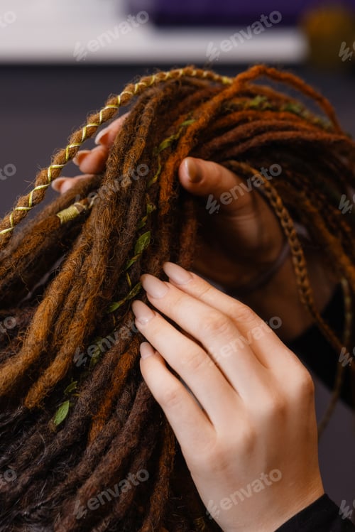 Vorschau: Hände flechten Dreadlocks mit Zierfäden aus nächster Nähe