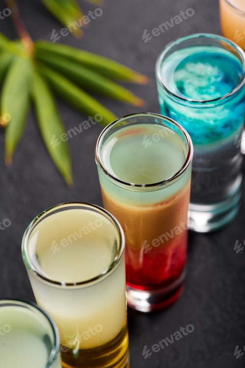 Preview: Row of shot cocktails at black slate table top. Alcoholic cocktails set. Tropical bar