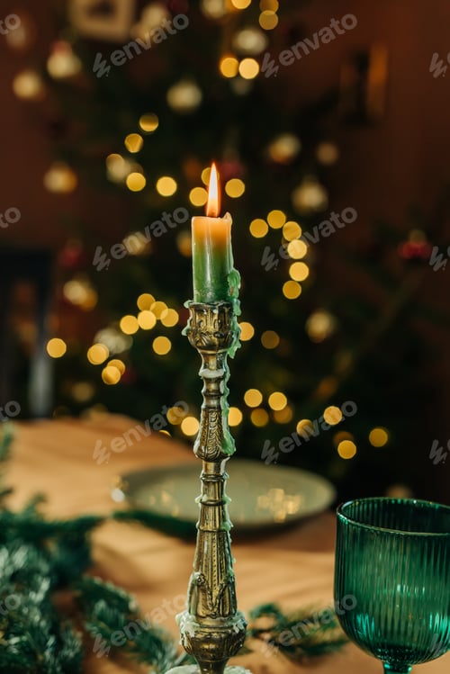 Preview: Christmas dinner set table with candles, glasses, plates, and tree in background.