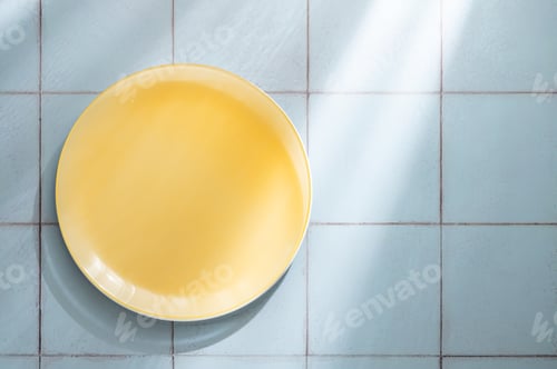 Preview: An empty yellow plate on a blue tile background with sunlight.