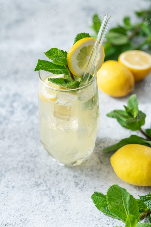 Preview: A summer drink with lemon, mint, and ice in a glass on a concrete background.