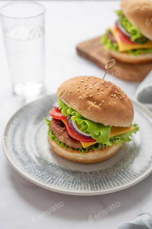 Preview: Two Beef burgers with tomato, cheese, and lettuce on a plate on a marble background