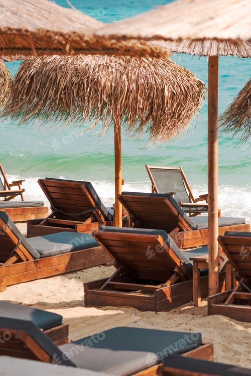 Preview: Wooden boardwalks on sand and shaded lounge chairs beneath rustic straw umbrellas by the sea, perfec