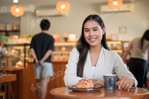 Preview: Smiling Thai businesswoman looking at camera at bakery cafe table with coffee
