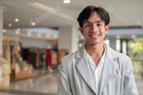 Preview: Smiling young nonbinary Thai business professional looking at camera in shopping mall