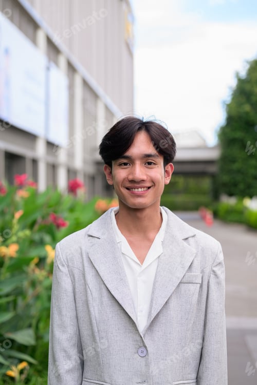 Preview: Smiling young nonbinary Thai business professional looking at camera outdoors on city path