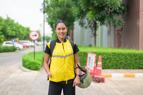 Preview: Full Length Female Delivery Courier Standing on Urban Sidewalk