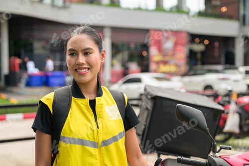 Preview: Horizontal Shot of Smiling Thai Female Delivery Courier Looking Away Next to Motorcycle