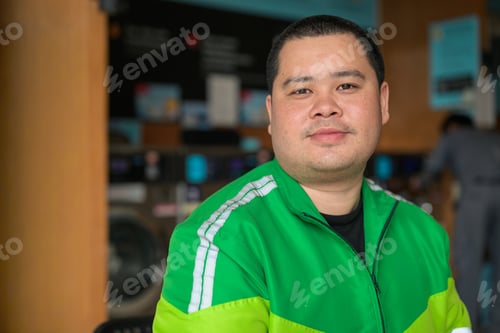 Preview: Plus size Thai courier in green uniform jacket looking forward inside modern laundry close up portra