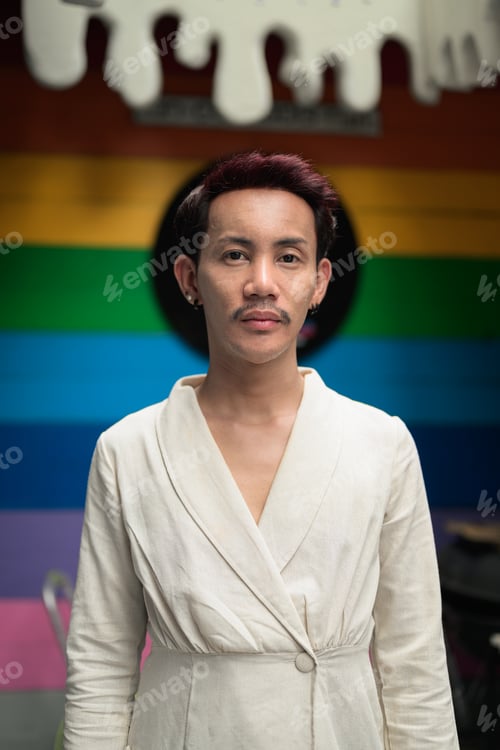 Preview: Non-binary gay Thai man from Isan standing before a colorful rainbow pride background, portraying au