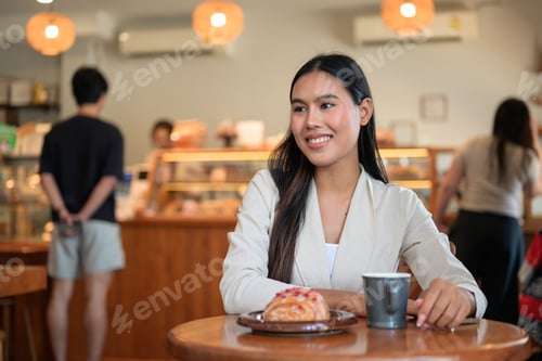 Preview: Smiling Thai businesswoman looking away at bakery cafe with coffee and pastry