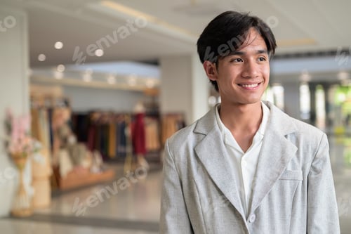 Preview: Smiling young nonbinary Thai business professional looking away in shopping mall