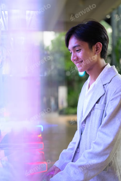 Vista previa: Smiling young nonbinary Thai business professional playing arcade claw machine game