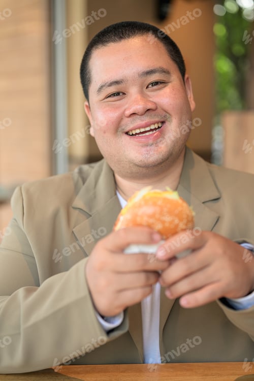 Preview: Plus size Isan Thai businessman looking at camera with a burger
