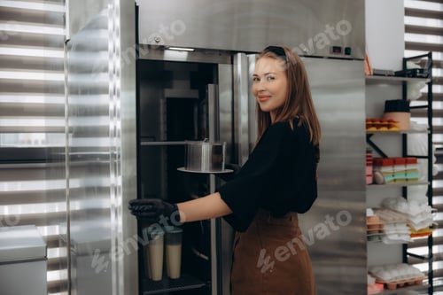 Preview: Woman chef storing food in professional kitchen refrigerator