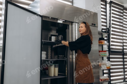 Preview: Woman chef checking products in commercial refrigerator