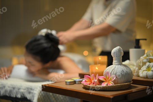 Preview: Focus on spa equipment and relaxing candlelight woman receiving traditional herbal compress massage