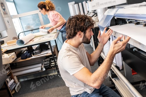 Preview: A print shop worker is servicing a printer, carefully inspecting and cleaning internal components.