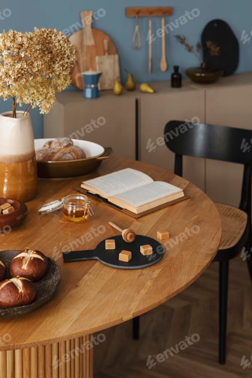Preview: Creative composition of dining room interior with round table, books, vase with flowers, bowl, bread