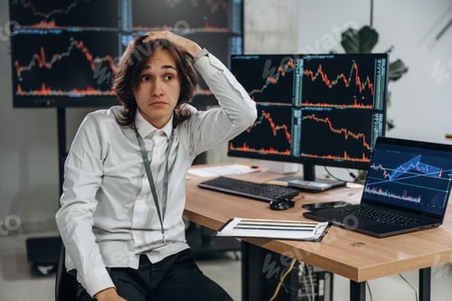 Preview: Young man is sitting in the office with multiple displays of stock market data