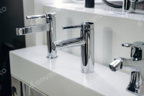 Preview: Modern chrome bathroom faucets displayed on a white countertop in a contemporary showroom, showcasin