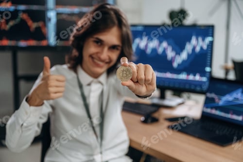 Preview: Golden colored crypto coin. Young man is sitting in the office with multiple displays of stock marke