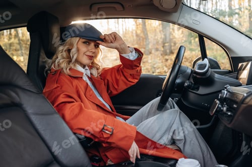 Preview: In red coat and blue beret. Happy blonde woman is sitting her electric car
